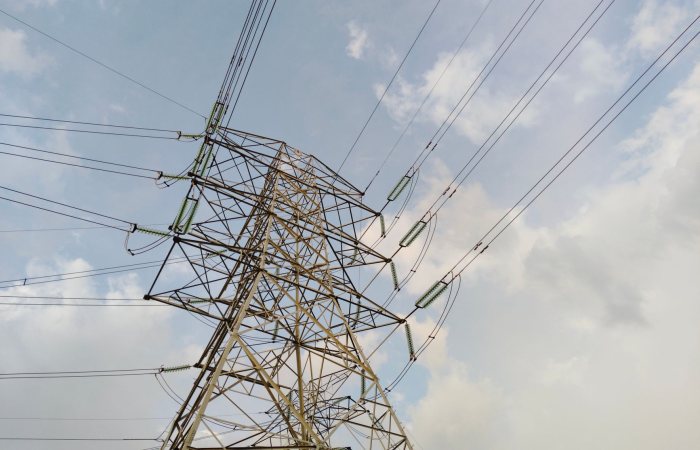 A close-up view of a high voltage transmission tower and lines against a cloudy sky.