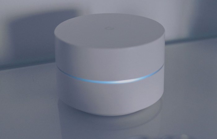 A clean and modern minimalist design of a white round electronic device with a blue light ring on a reflective glass surface.