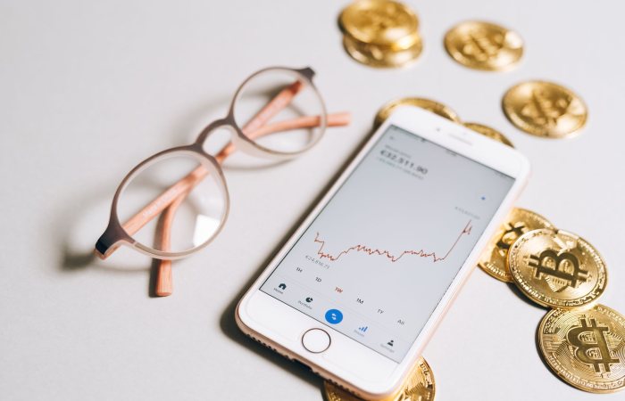 Smartphone displaying cryptocurrency graph alongside bitcoin coins and eyeglasses.
