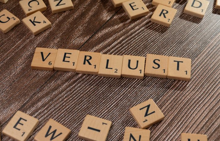 Scrabble tiles spelling 'Verlust' on a wooden table, symbolizing loss or financial context.