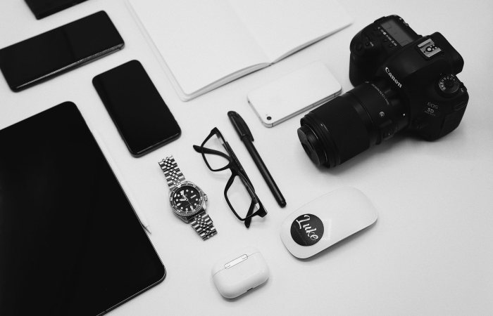 A flat lay of modern tech gadgets including a camera, smartphone, and tablet on a minimalist white desk.